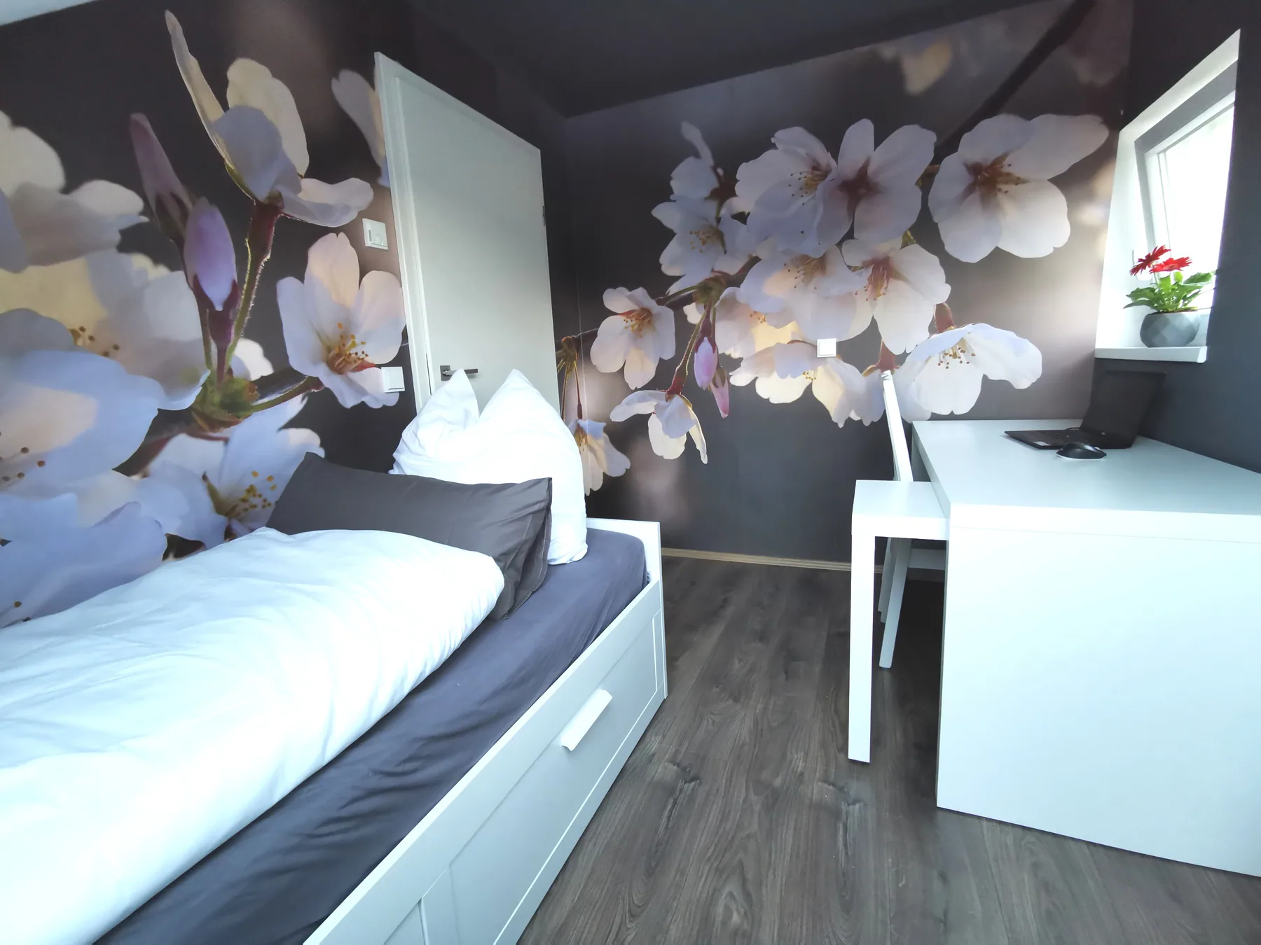 Gästezimmer mit ausziehbarem Bett, Schreibtisch und Blütenmotiv